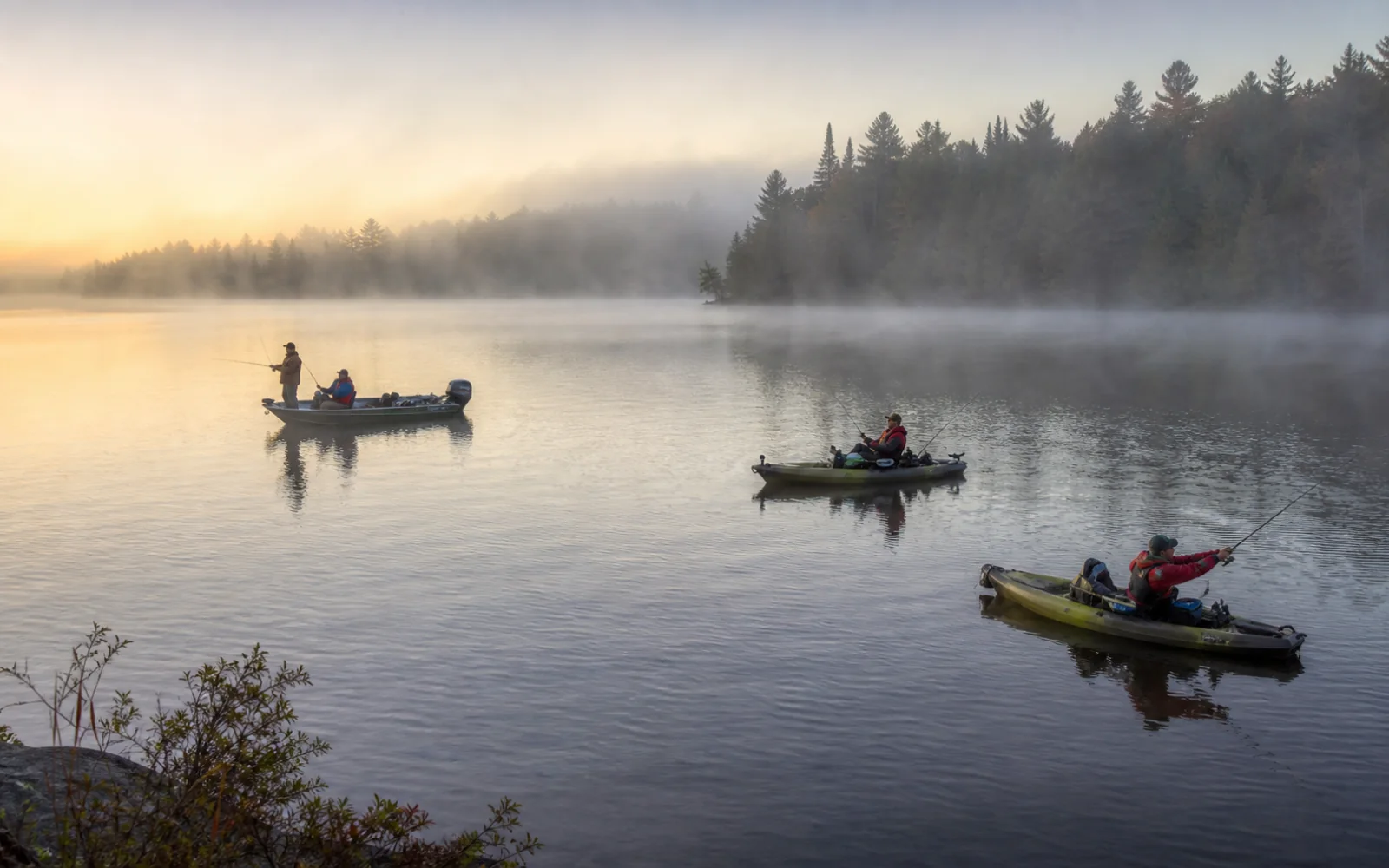 Boat and kayak anglers fishing together on a misty lake